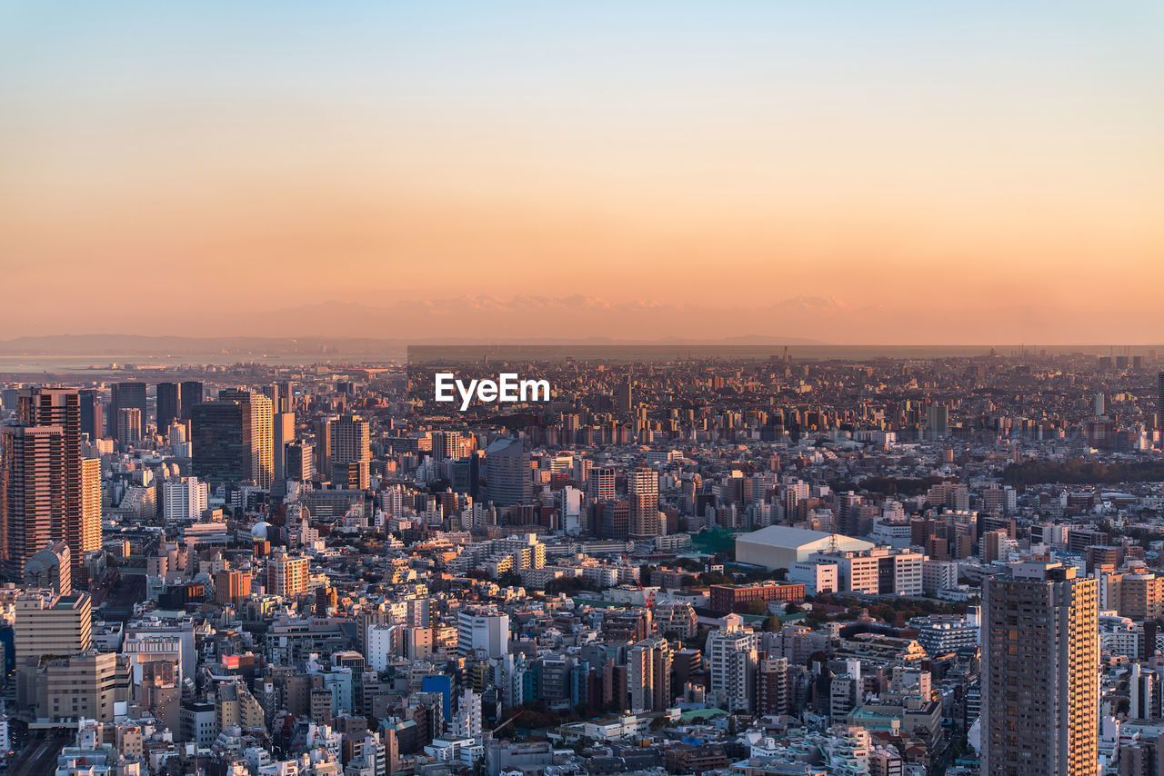 HIGH ANGLE VIEW OF ILLUMINATED CITY BUILDINGS AGAINST SKY DURING SUNSET