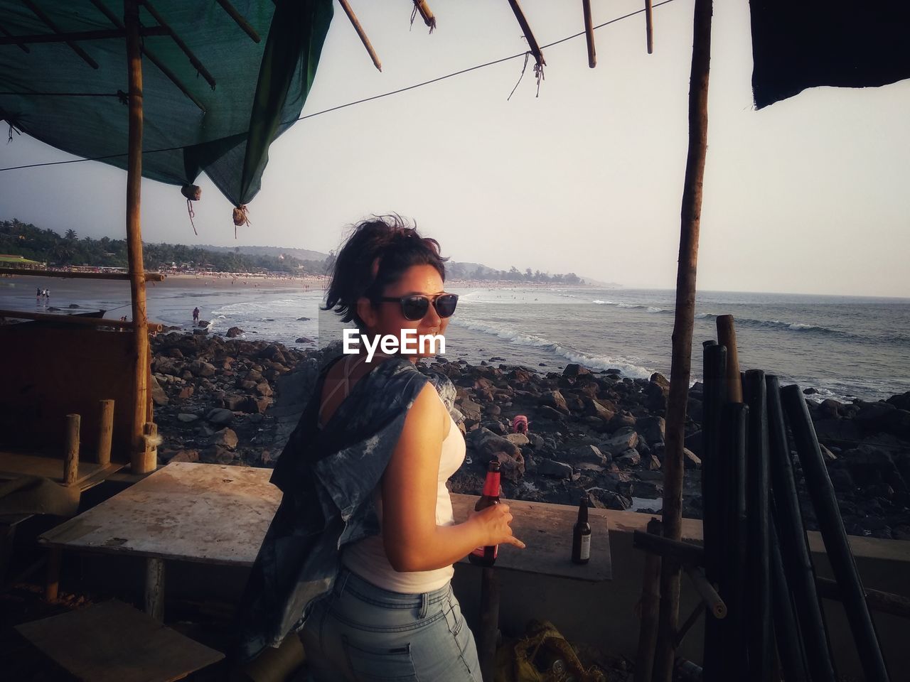 Young woman standing at beach against sky