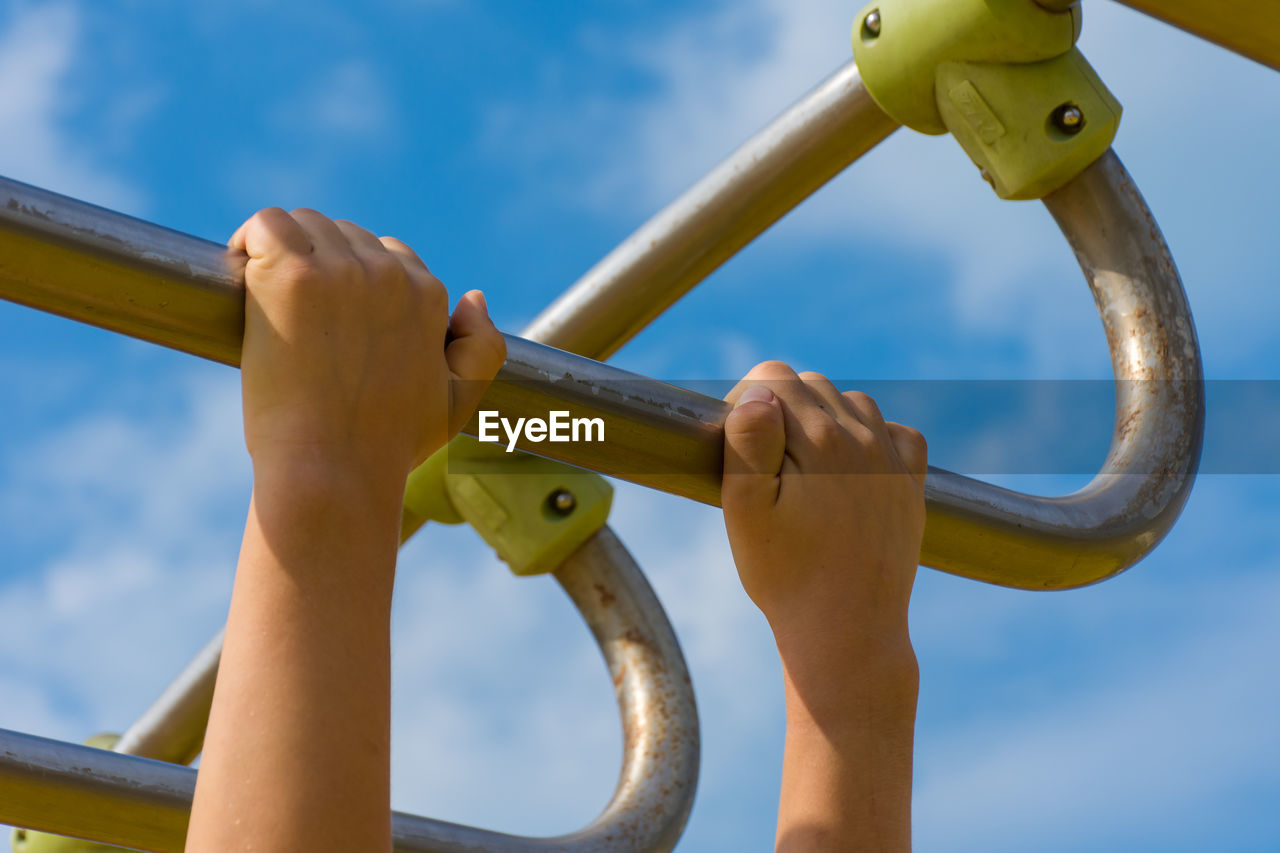 Low angle view of hand holding metal against sky