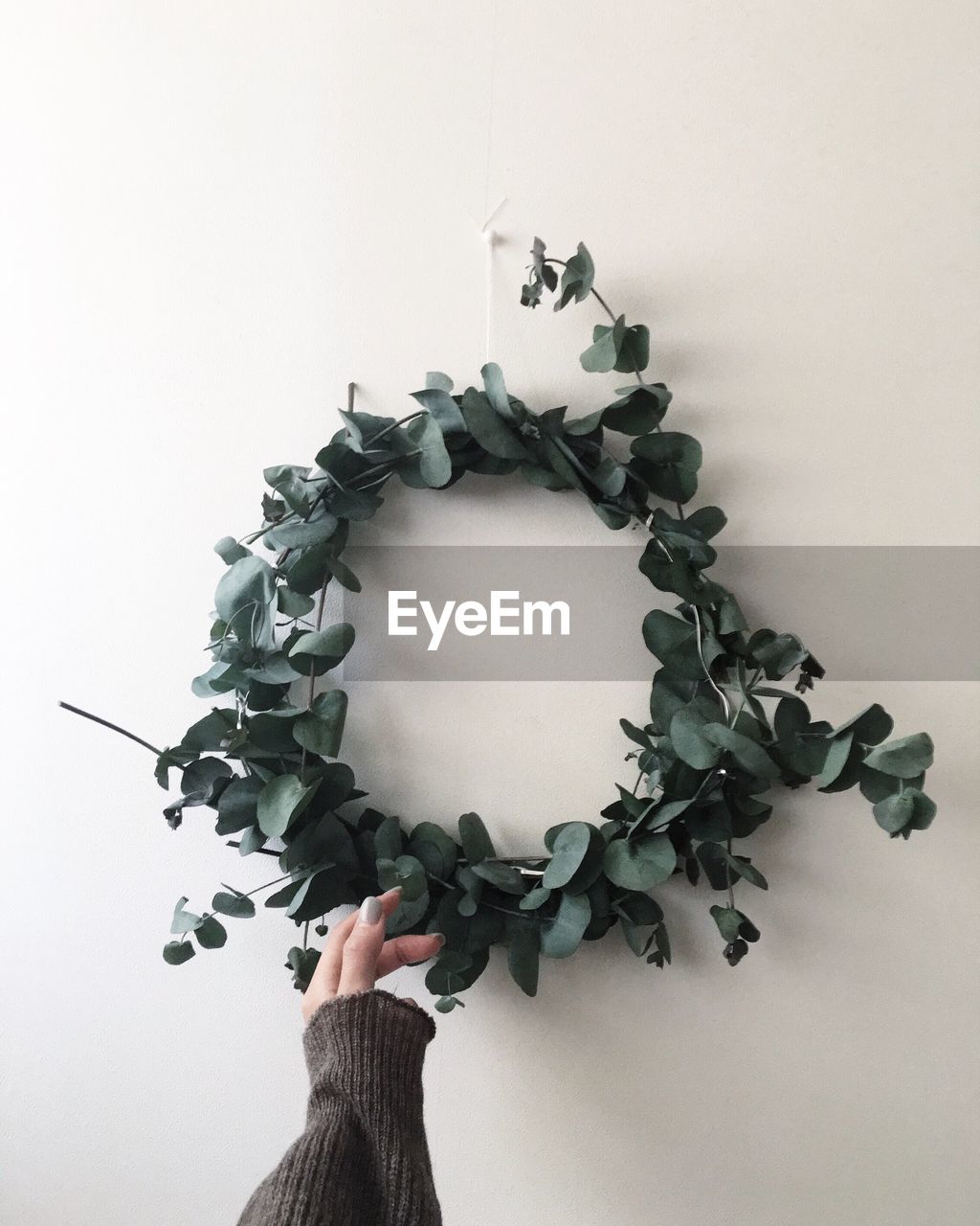 Cropped image of woman touching wreath at wall