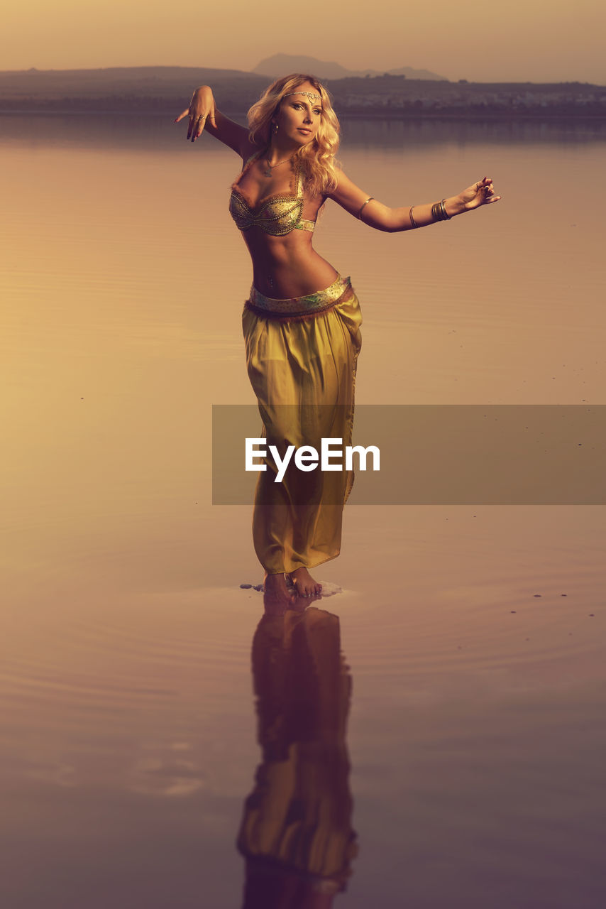 Young woman standing at beach during sunset