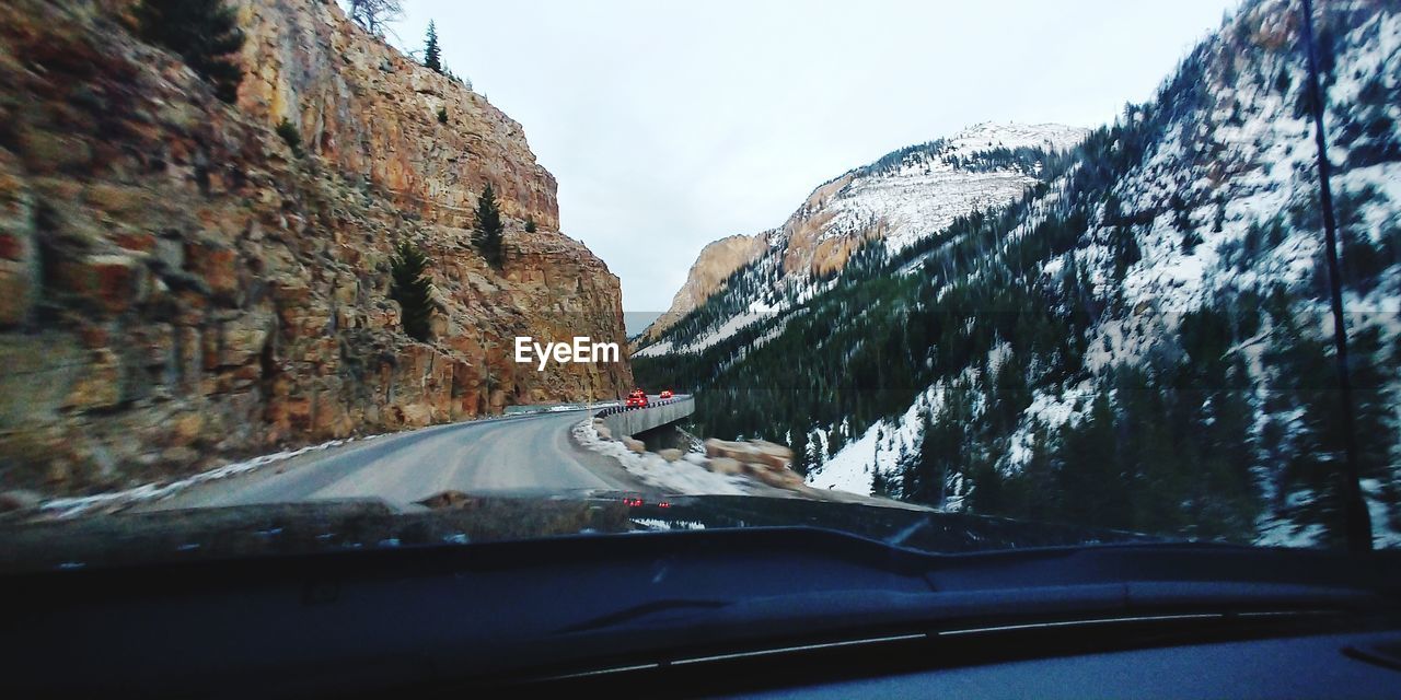 Road amidst snowcapped mountains seen through car windshield