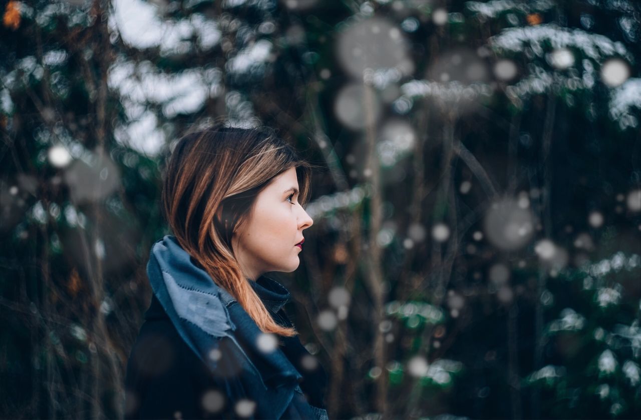 Profile view of thoughtful young woman standing against trees