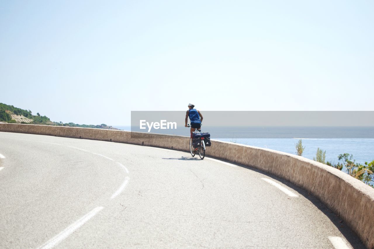 Rear view of man riding bicycle on road against sky