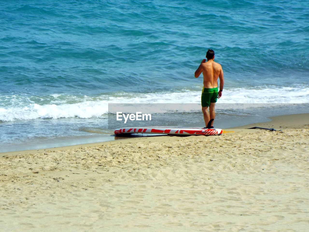Rear view of man standing by surfboard on beach