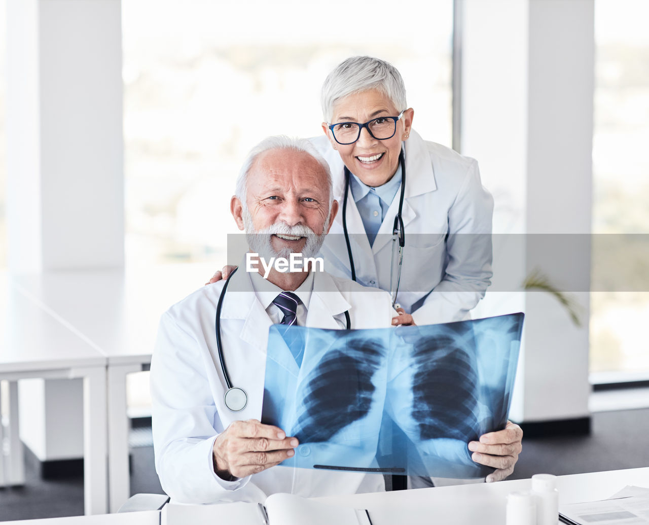 Portrait of smiling senior doctor holding medical x-ray by colleague in hospital