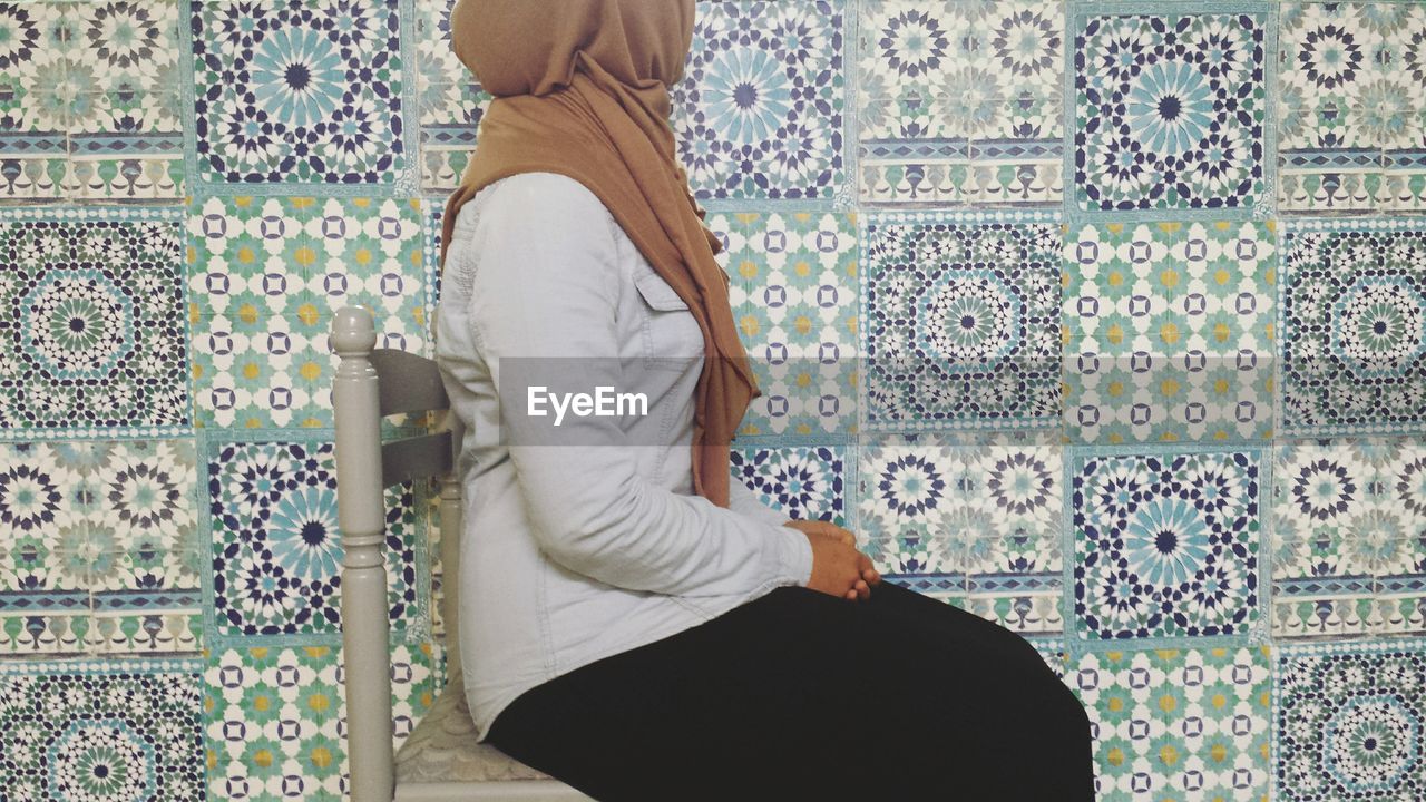 Low section of woman sitting against tiled wall