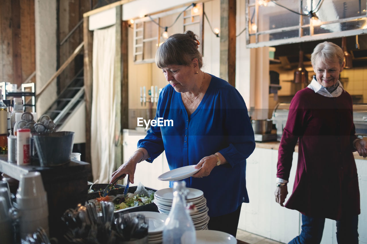 Senior woman looking at female friend taking food in plate at restaurant