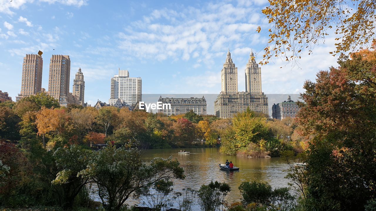 Trees and buildings by river against sky