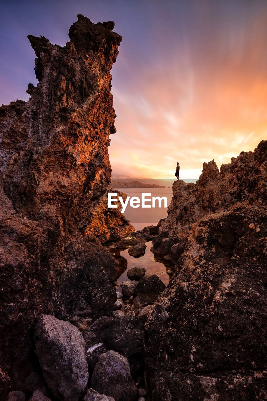 Man standing on rock formation against sky during sunset