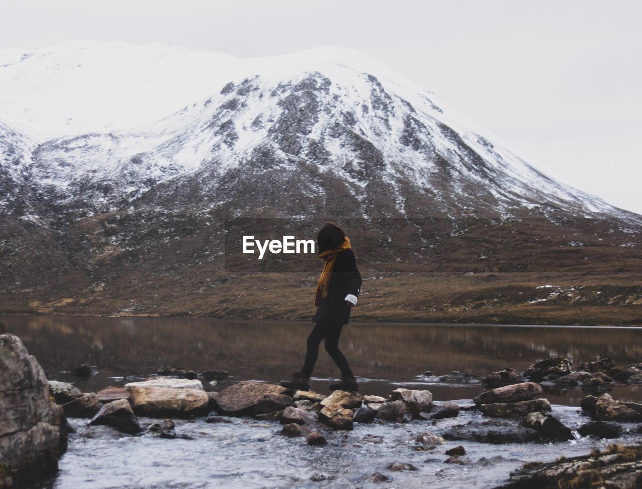 Woman walking at lakeshore against snowcapped mountains