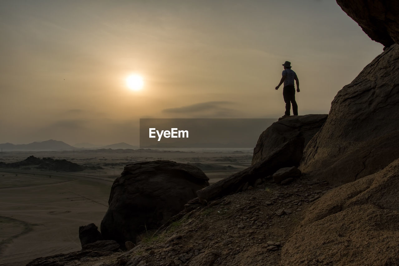 MAN STANDING ON ROCK AGAINST SKY