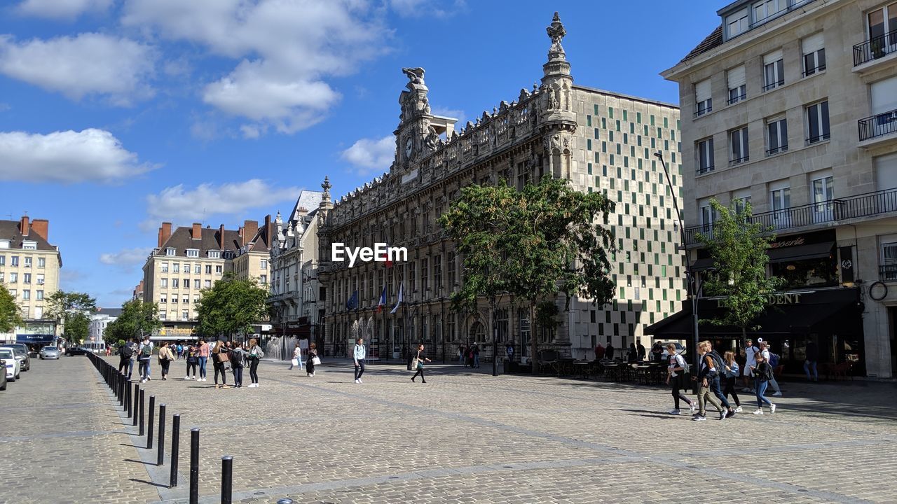 People on street amidst buildings in city against sky