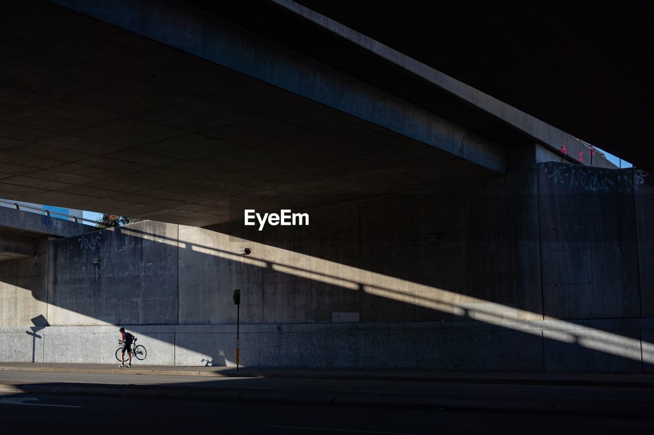 Man with bicycle walking under bridge in city