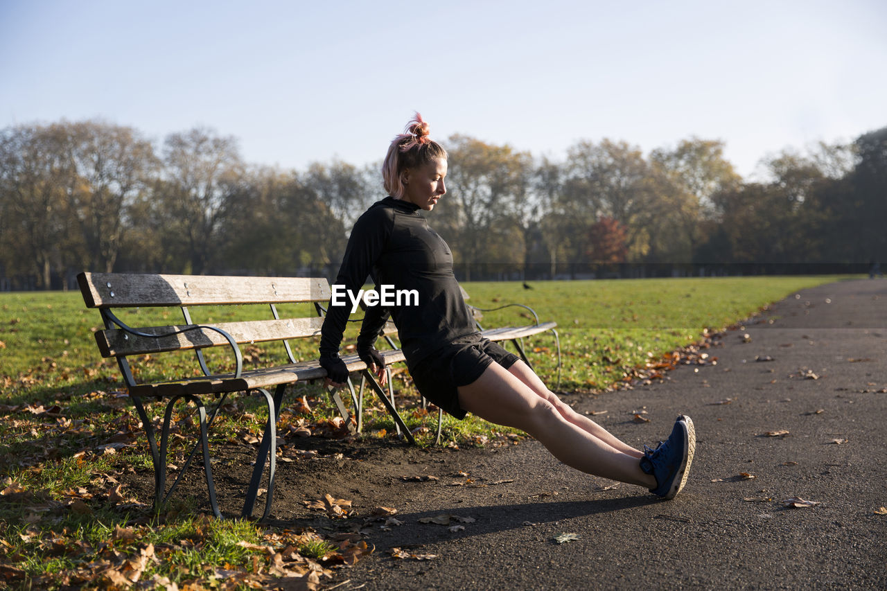 Full length of woman exercising by park bench