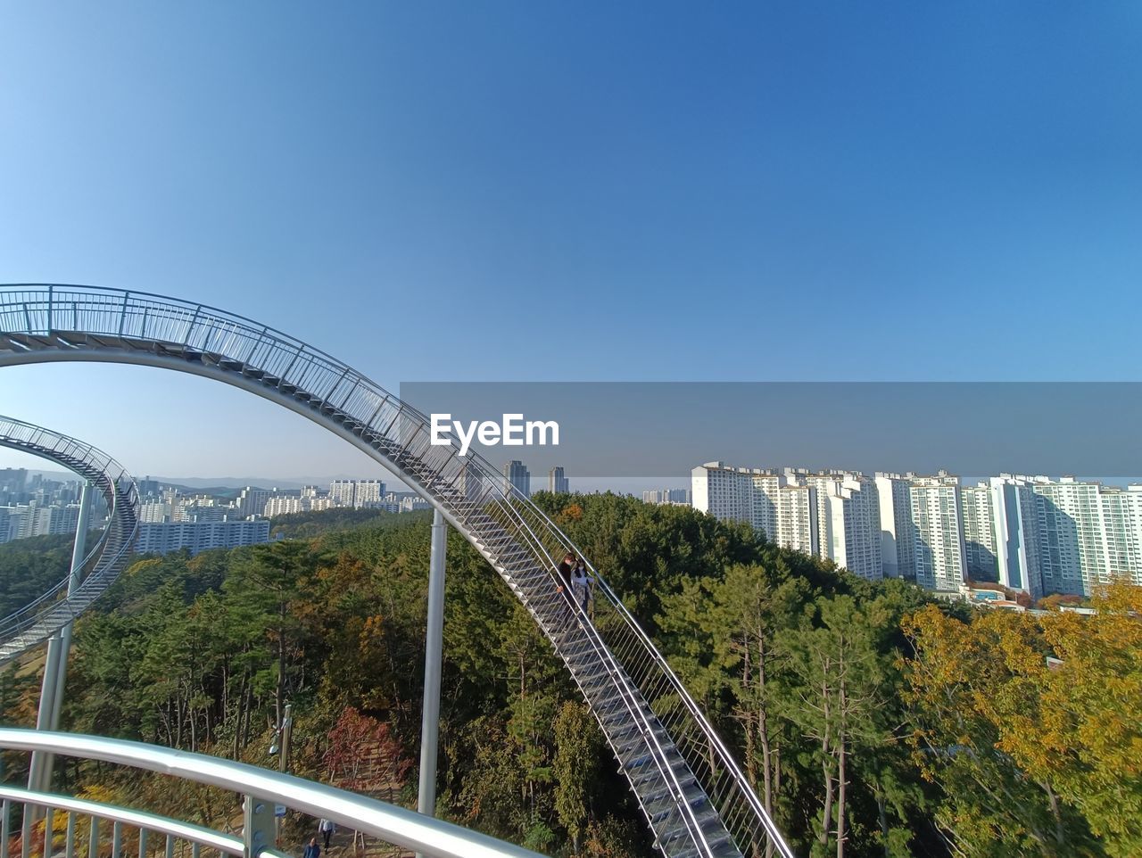 architecture, built structure, bridge, city, sky, landmark, nature, transportation, building exterior, cityscape, travel destinations, blue, no people, landscape, travel, arch bridge, tree, clear sky, outdoors, building, transport, park, day, road, plant, environment, cable-stayed bridge, roller coaster, metropolitan area, overpass, curve, motion, sunny, amusement park, urban skyline, skyscraper, tourism, office building exterior, scenics - nature, copy space, water, business finance and industry, highway