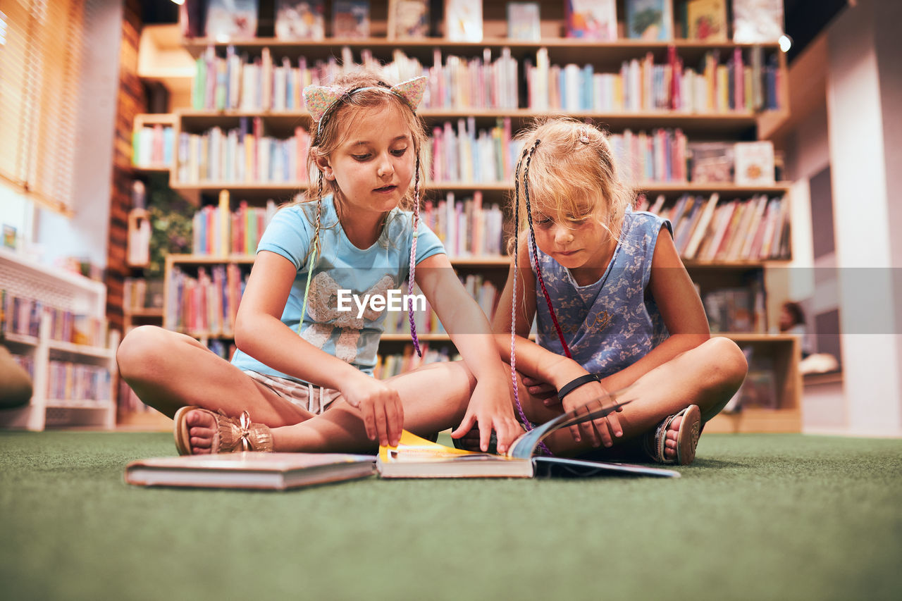 Two schoolgirls reading books in school library. primary school students learning from books