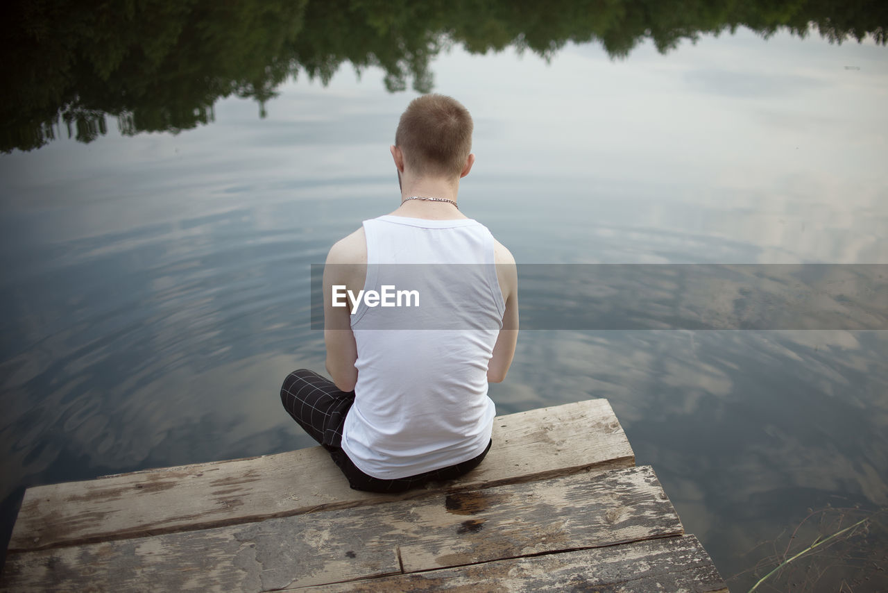 REAR VIEW OF SENIOR MAN SITTING ON LAKE