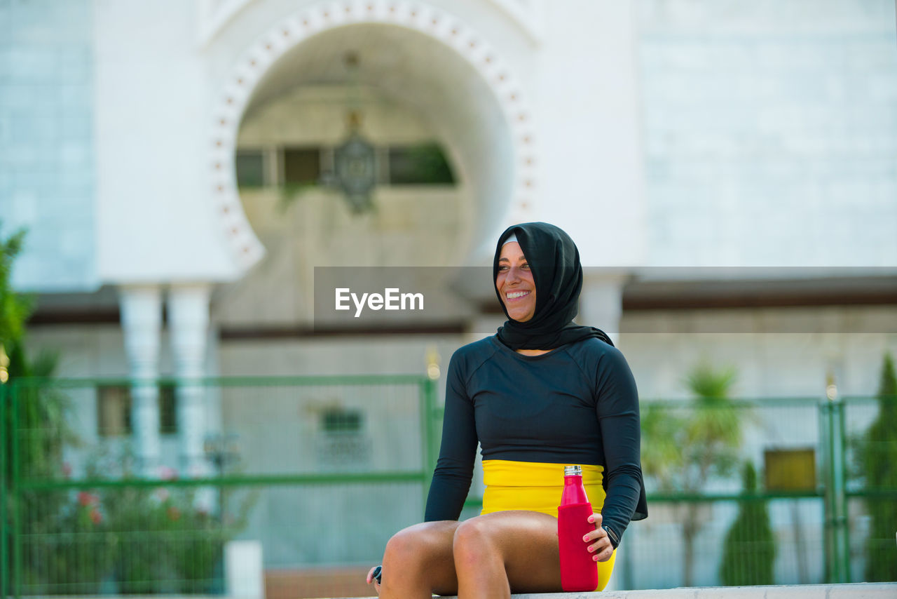 Smiling woman in hijab looking away while sitting outdoors