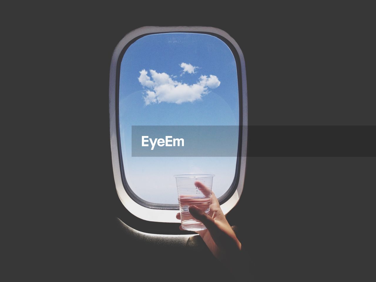 Close-up of hand holding glass of water in front of airplane window