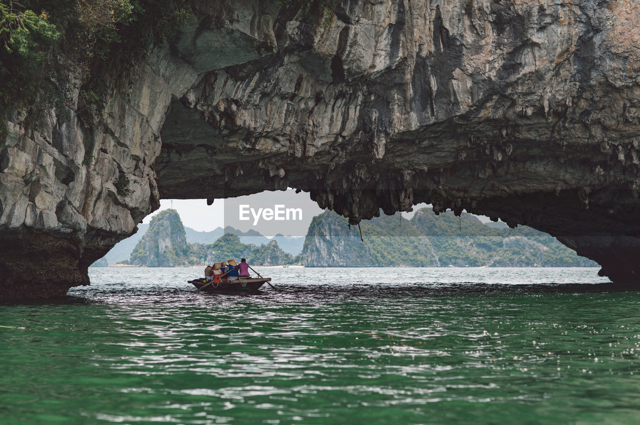 People rowing boat on halong bay under rock formation