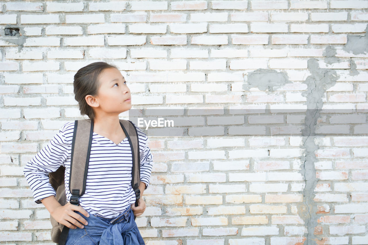 Young girl standing against brick wall