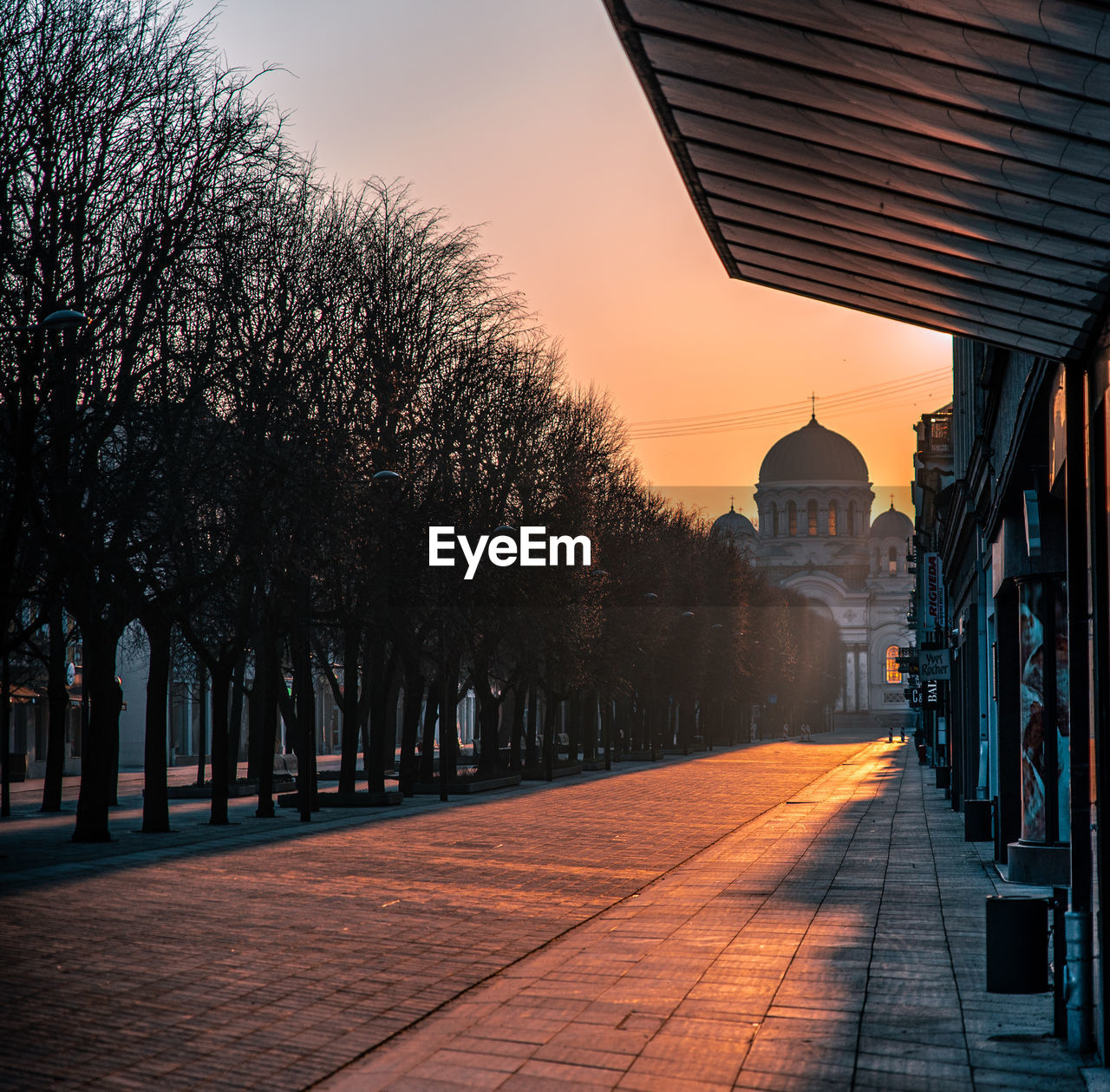 STREET AMIDST BUILDINGS AGAINST SKY AT SUNSET