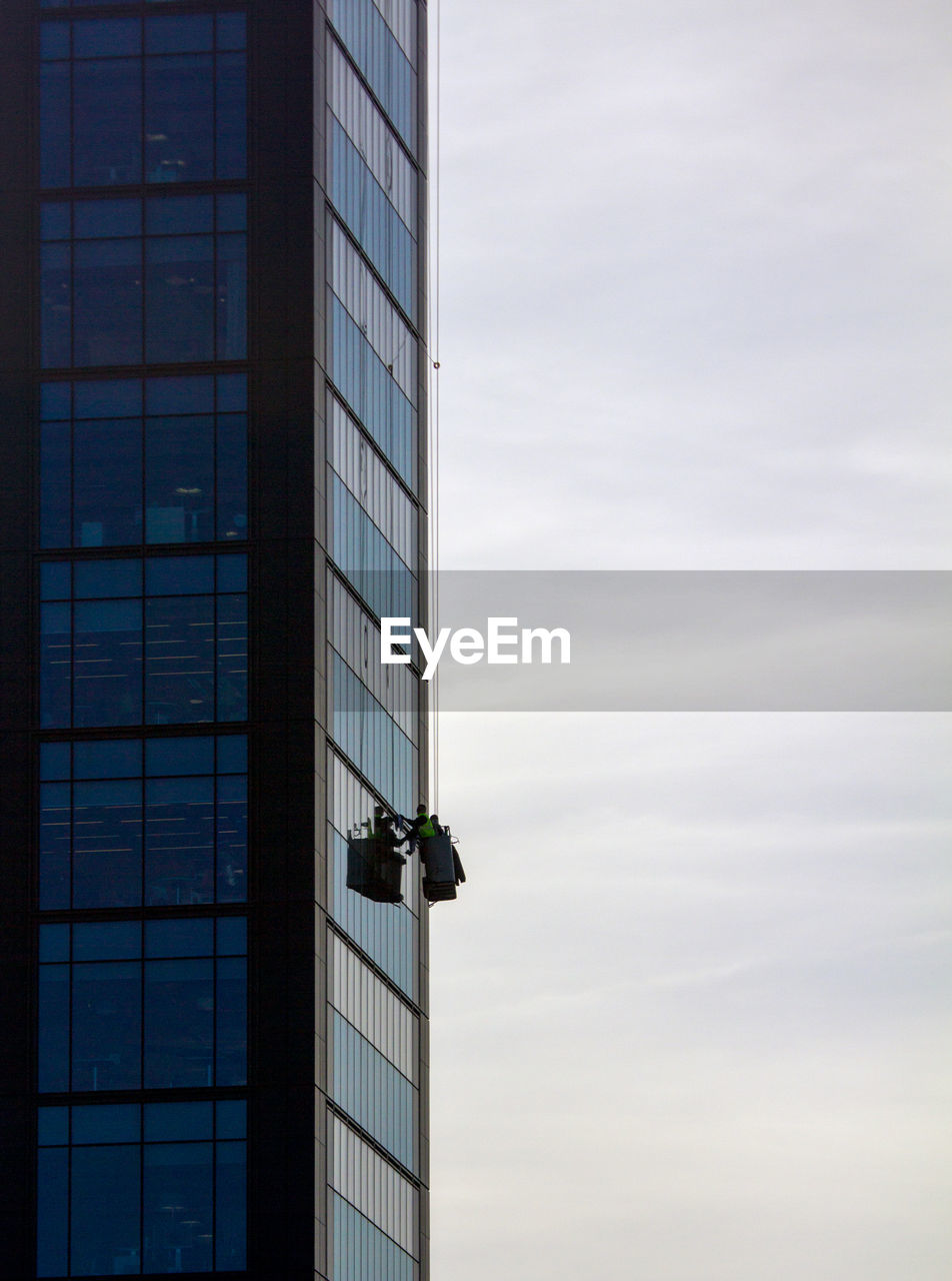 Low angle view of window washer against cloudy sky