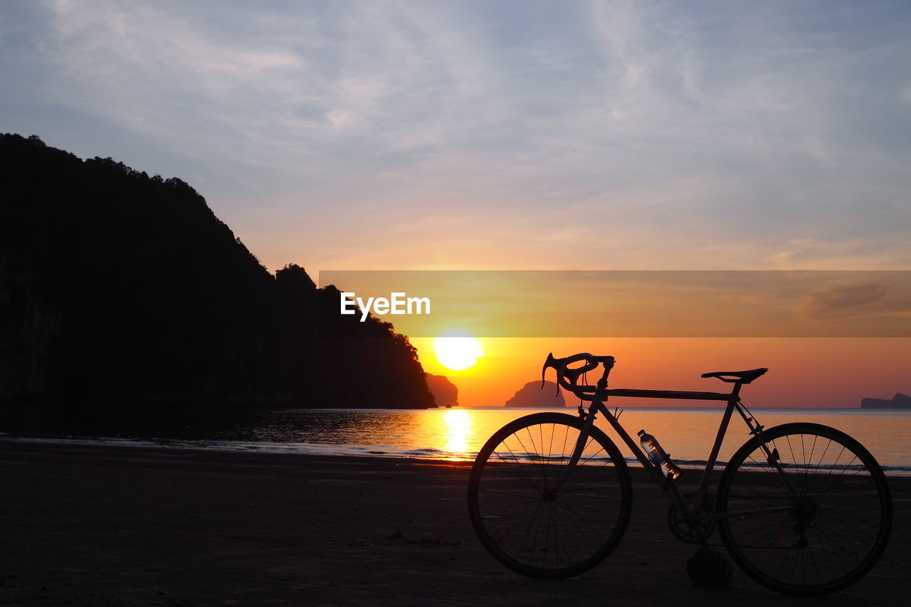 Silhouette bicycle on beach against sky during sunset