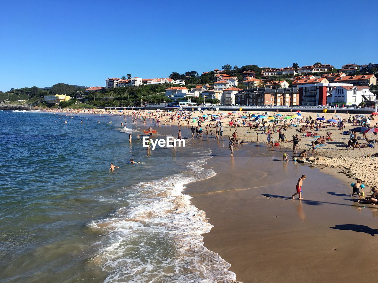 People at beach against clear blue sky