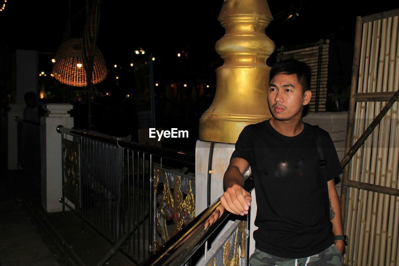 Portrait of young man standing against railing at night