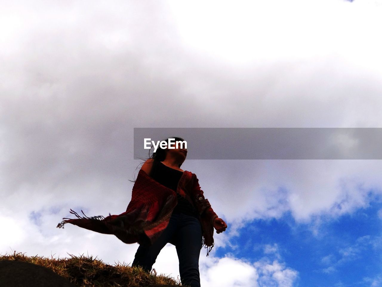 Low angle view of woman standing on cliff against cloudy sky