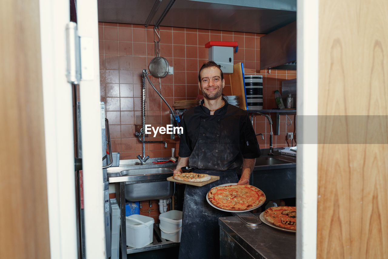 Portrait of young male chef preparing italian pizza in kitchen