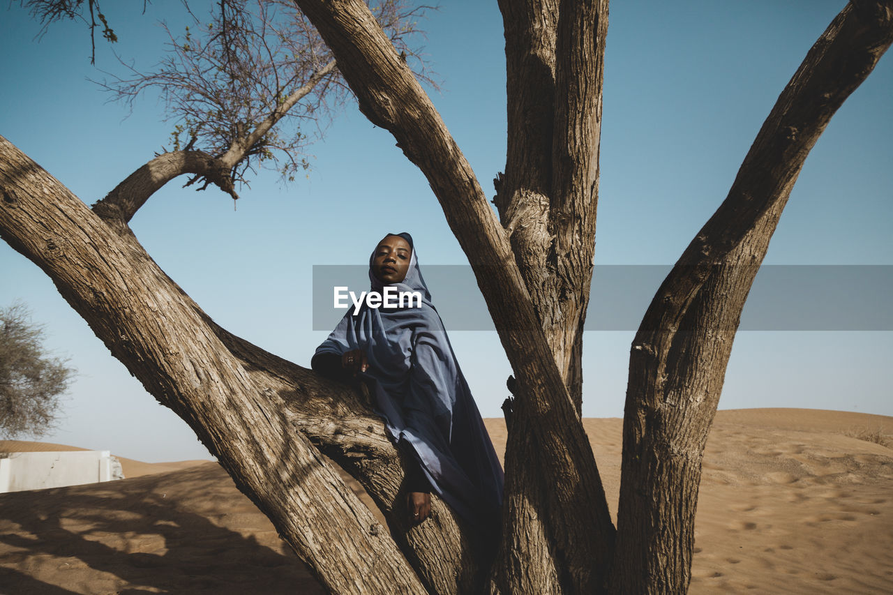 FULL LENGTH OF MAN SITTING ON TREE TRUNK