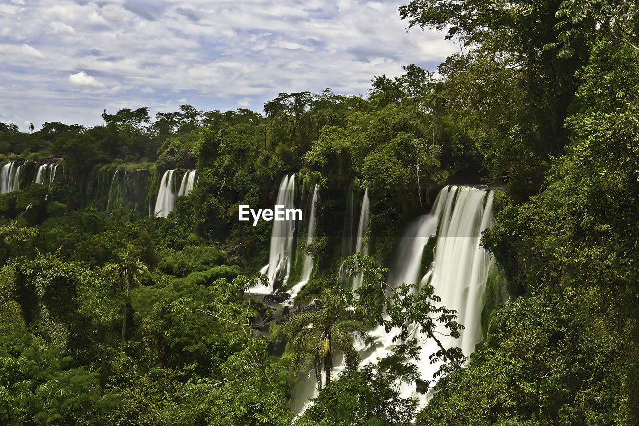 Scenic view of waterfall in forest against sky