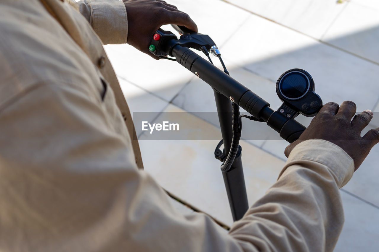 High angle of crop unrecognizable ethnic male standing on modern electric scooter while using gas and break on handlebar