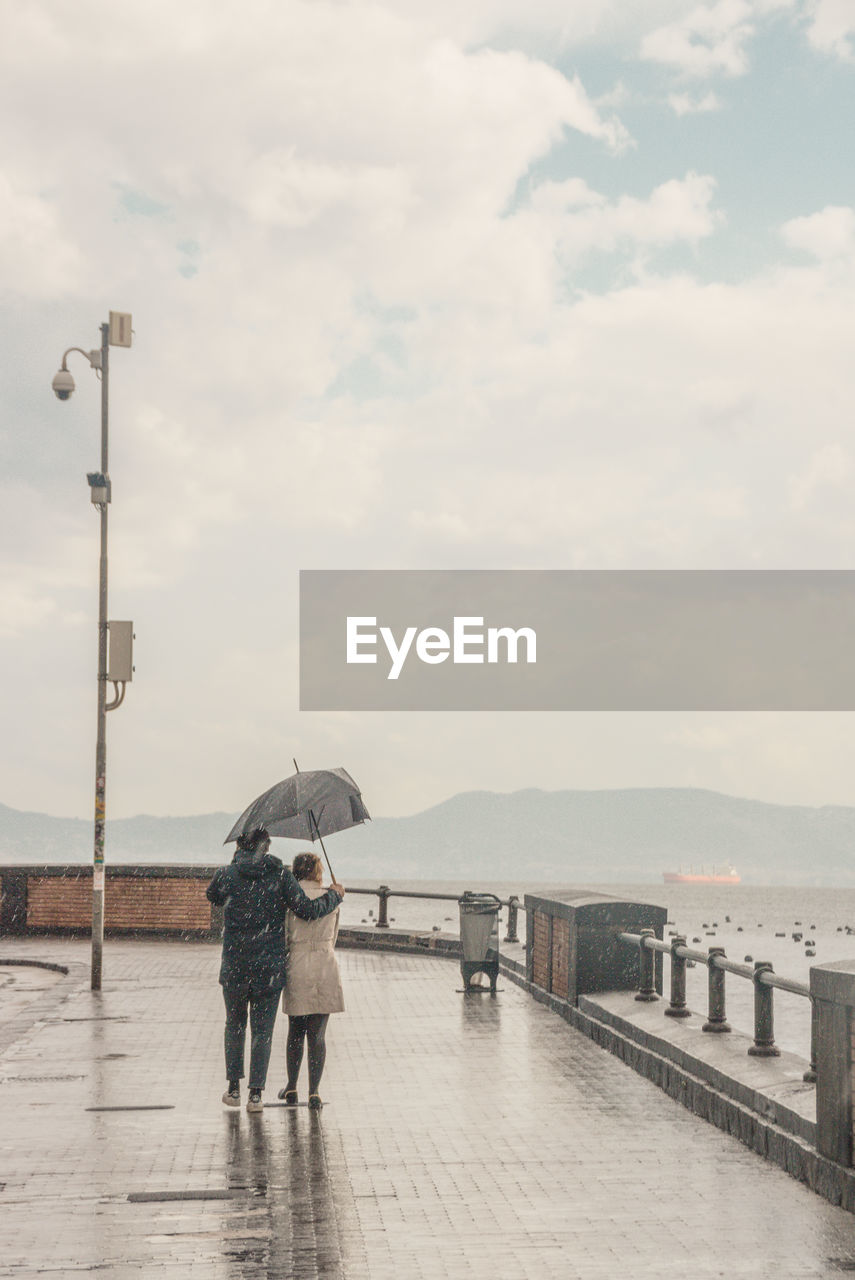 Rear view of couple with umbrella on street during rainy season