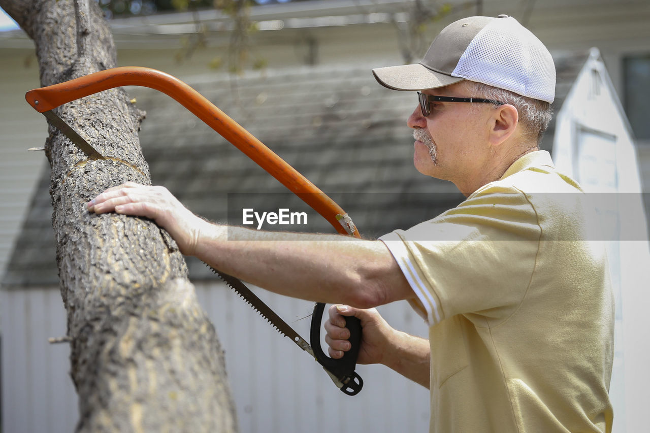 Side view of senior man sawing tree outdoors