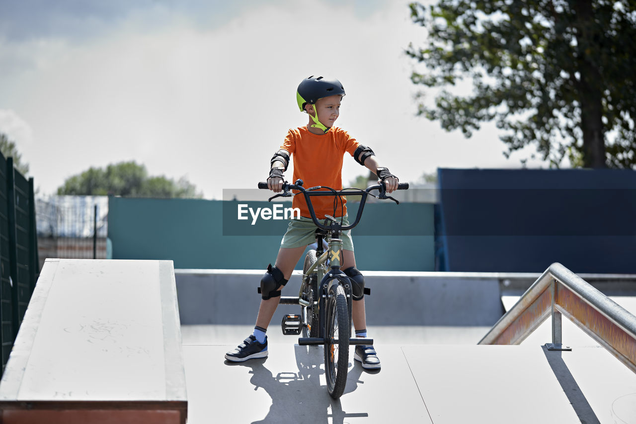 Boy with protective gears sitting on bmx bike at skateboard park