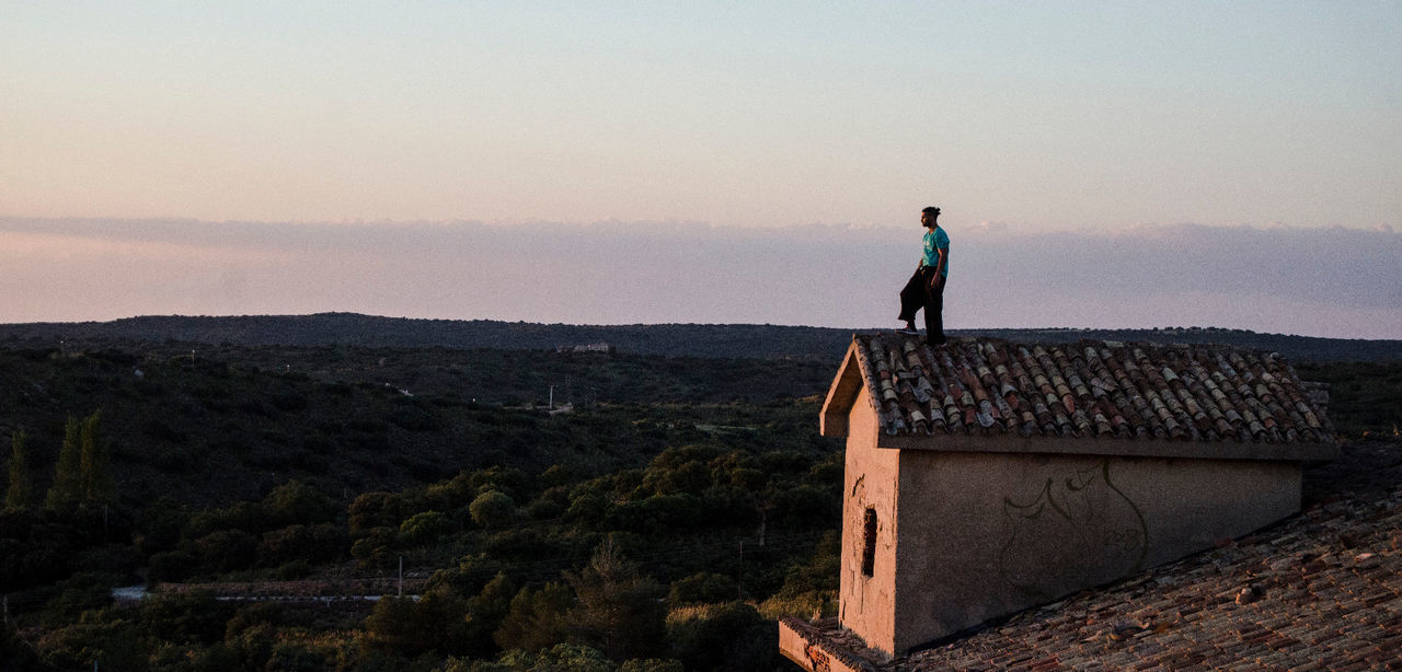 Side view of man standing on roof against mountain