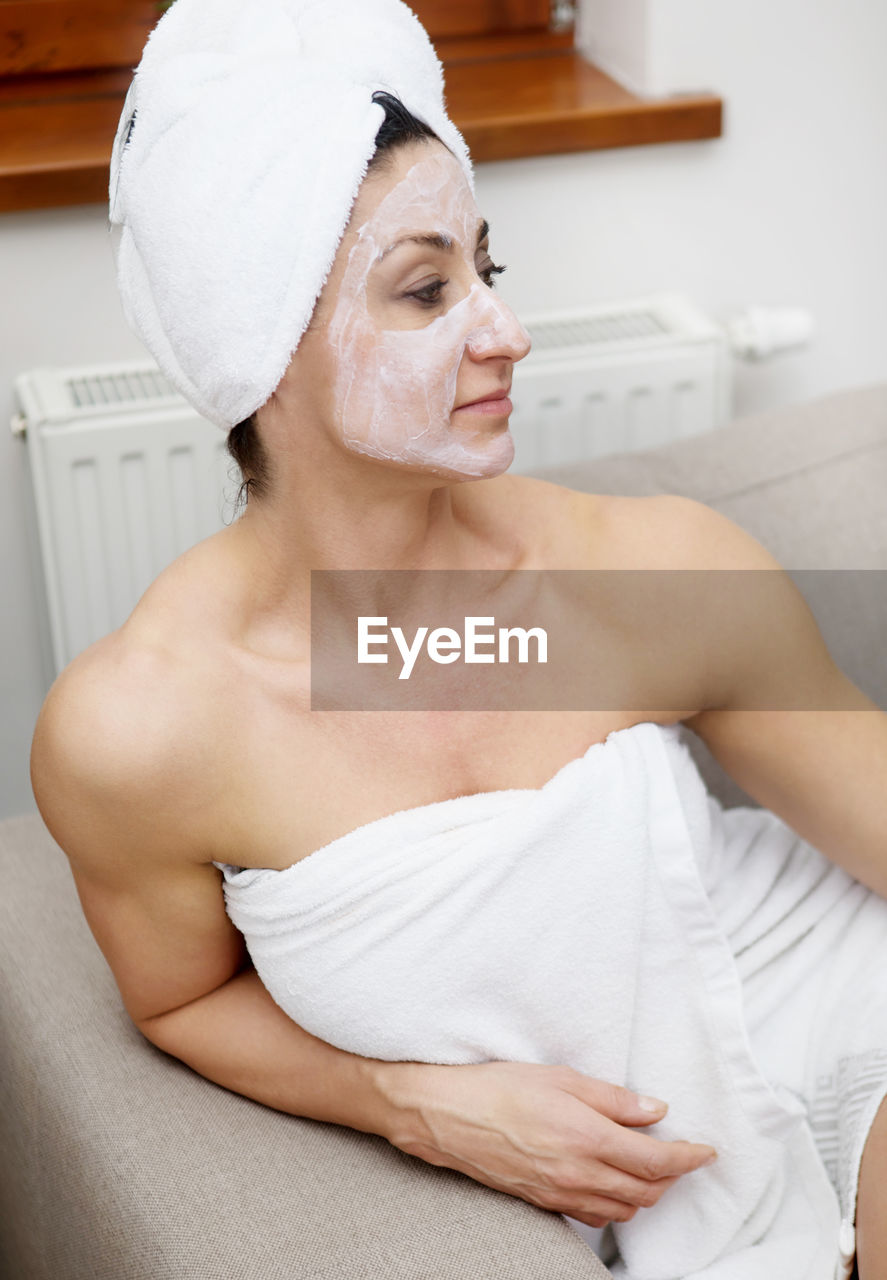 Woman with face mask sitting on sofa at home