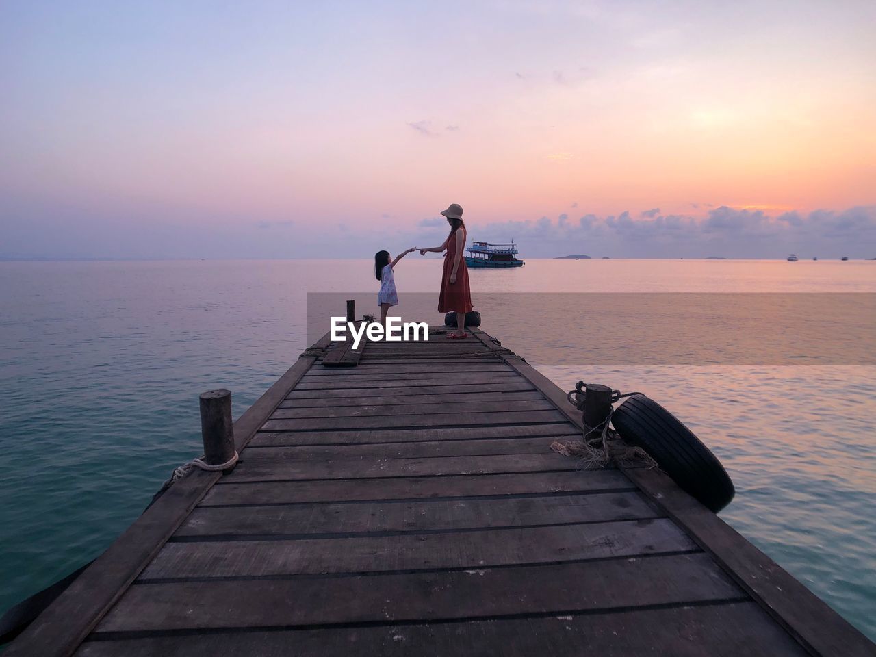 Side view of mother with daughter standing on pier over sea against sky during sunset