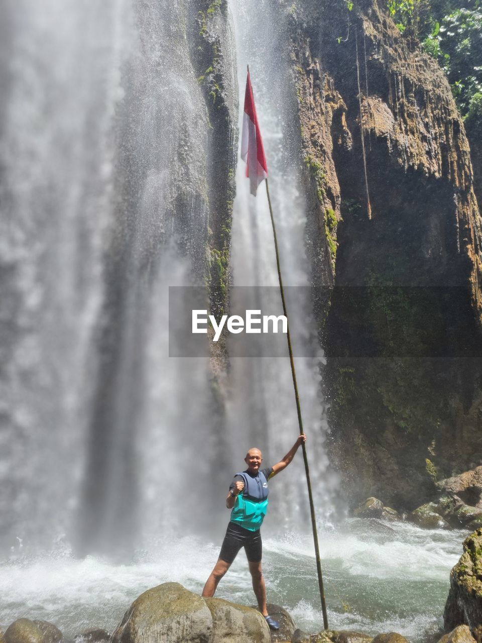 Low angle view of man standing front of waterfall