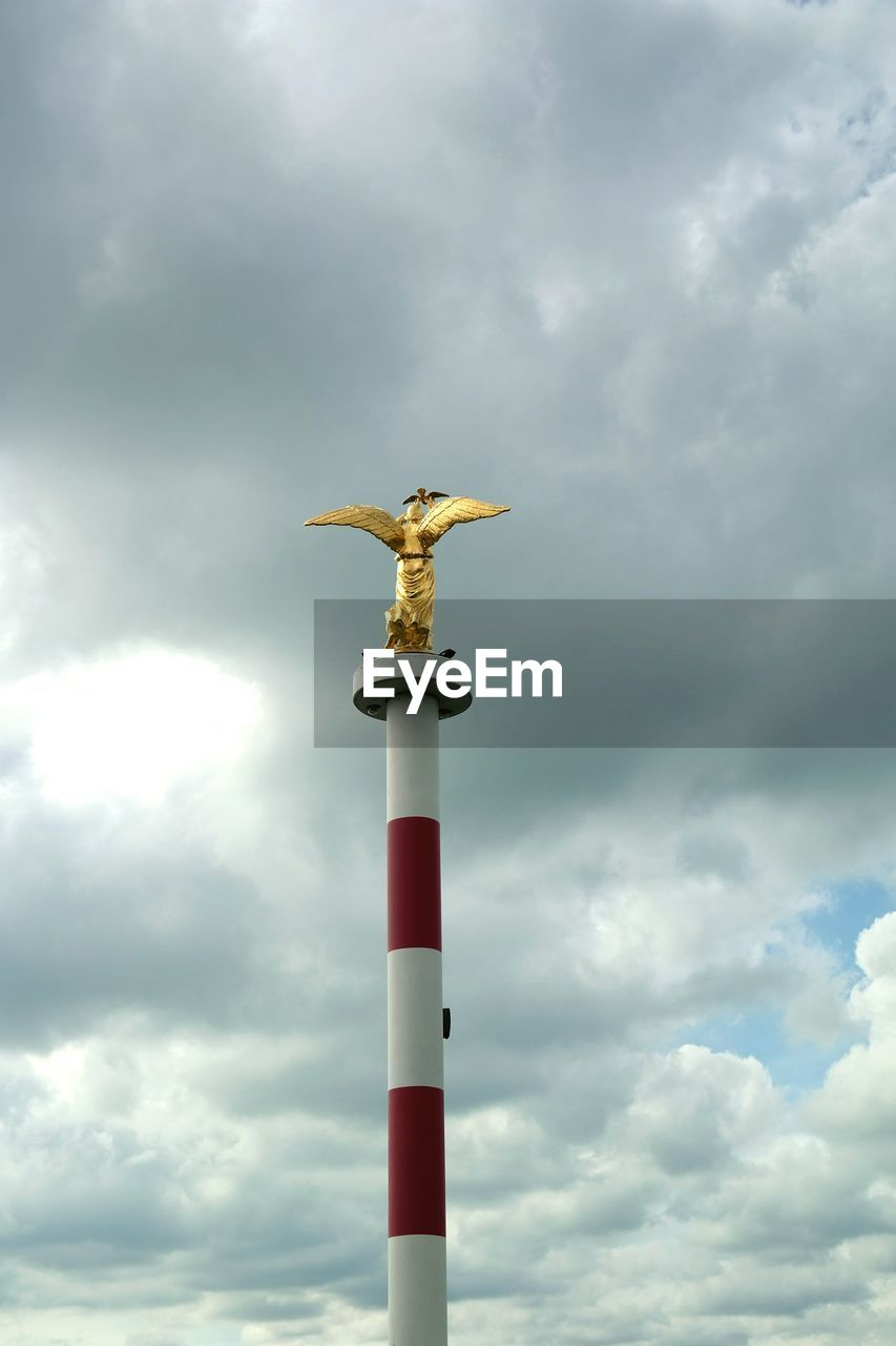 Low angle view of angel statue on pole against cloudy sky