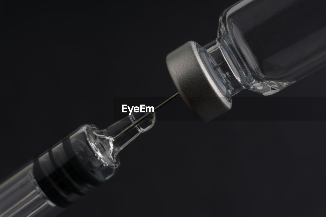 Close-up of syringe and vial against black background