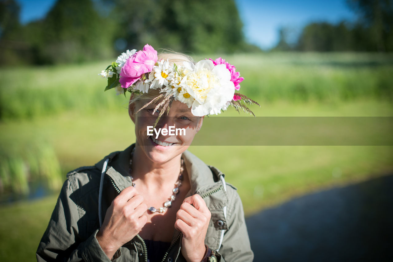 Portrait of smiling woman wearing flowers by field