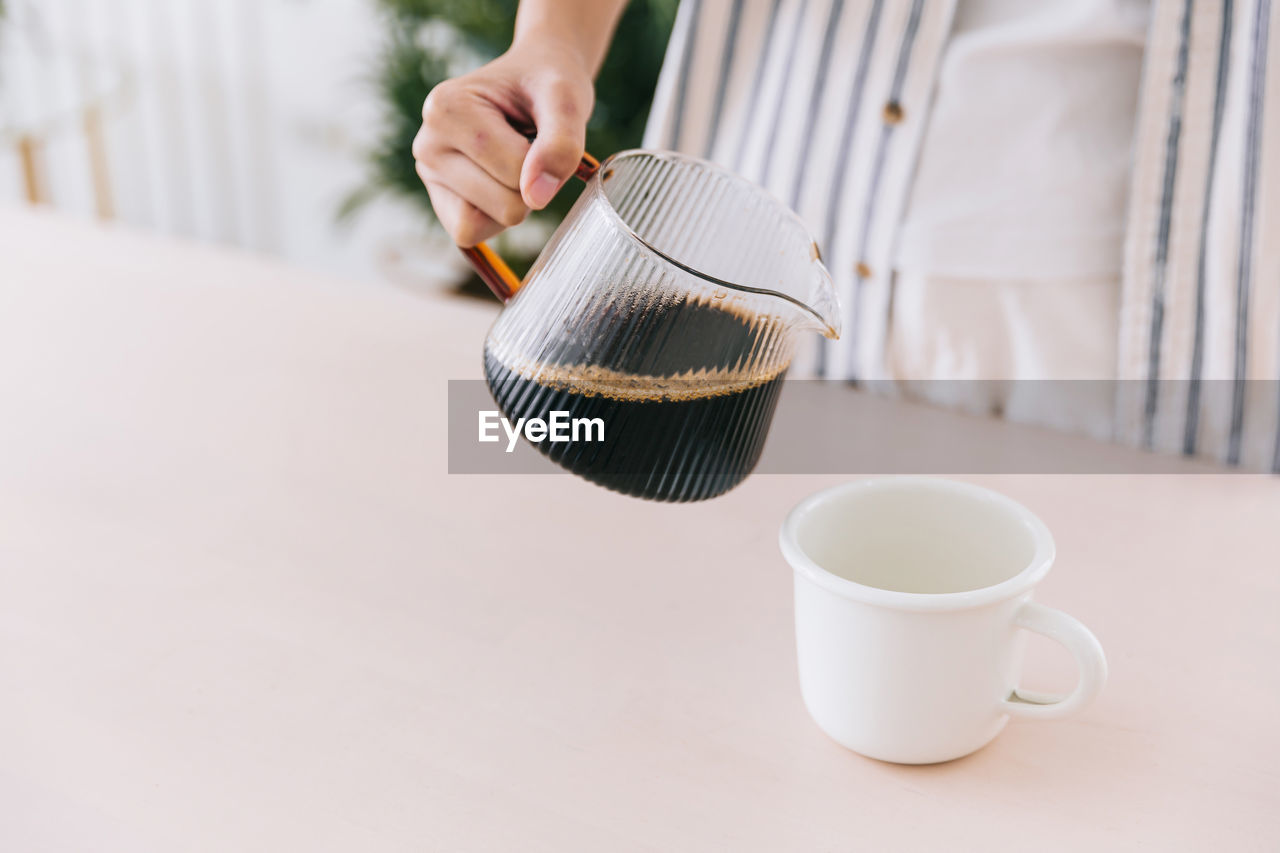 Close up professional barista hand pouring freshly brewed drip coffee in a white mug.