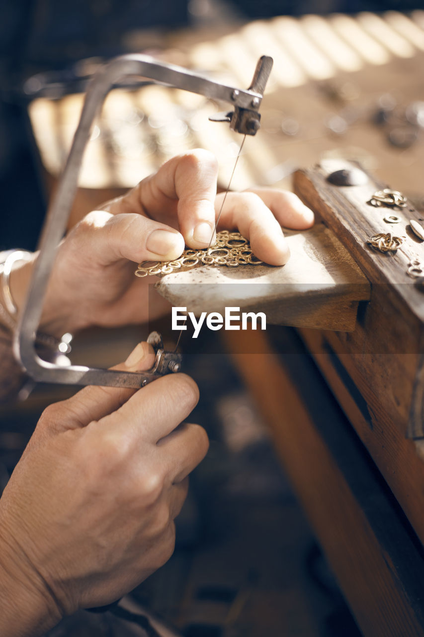 Cropped image of female goldsmith using saw while making jewelry in workshop