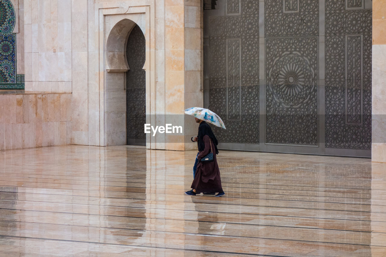 Couple with umbrella walkibg in hassan ii mosque square in a rainy day 
