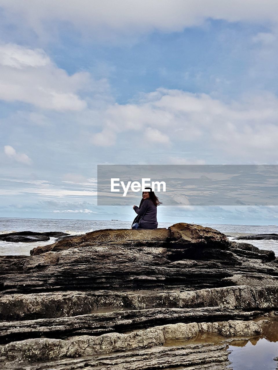 Rear view of woman sitting on rocks at sea against sky